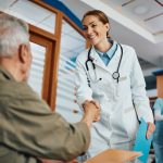 Happy doctor handshaking with her senior patient in waiting room at the clinic.
